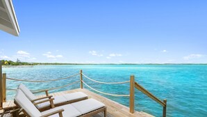 A wooden deck with two lounge chairs facing a turquoise sea under a clear sky. - Overwater Bungalow at Georgetown (Exuma)