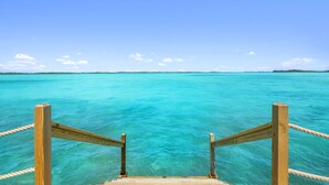 A wooden staircase leading into clear turquoise water with a distant landmass under a clear sky. - Overwater Bungalow at Georgetown (Exuma)