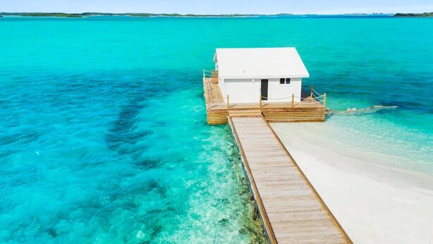 A white overwater bungalow with a wooden deck, surrounded by clear turquoise water. - Overwater Bungalow at Georgetown (Exuma)