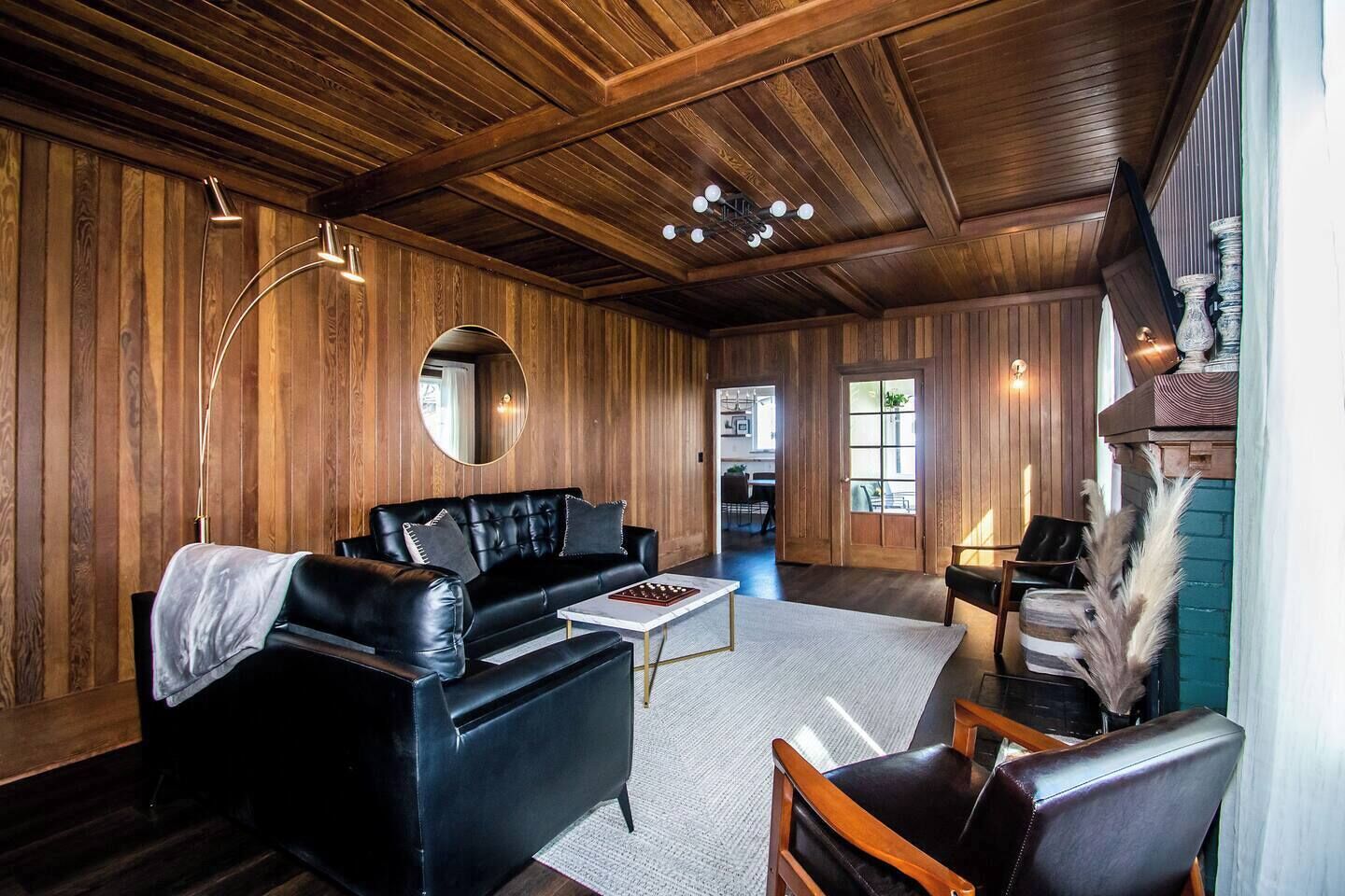 A cozy room with a black leather sofa, a round mirror, and a wooden ceiling.