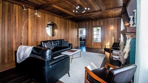 Une pièce chaleureuse avec un canapé en cuir noir, un miroir rond et un plafond en bois.