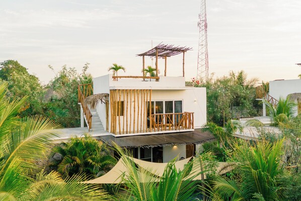 A modern, multi-story building with a wooden deck and a thatched roof structure.