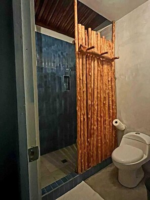 A bathroom with a toilet, a wooden partition, and a blue-tiled shower area.