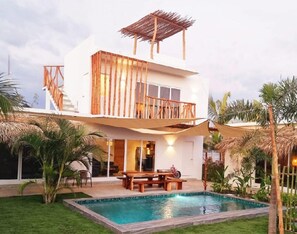 A two-story house with a pool, wooden deck, and a covered outdoor seating area.