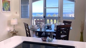 A kitchen with a glass-top table, a built-in stovetop, and a view of the ocean through large windows. - #26 Beach Apartment 2br, 3ba w/ jet tub (Isabela)