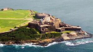 Vista aerea di un’antica fortificazione con una torre centrale, circondata da mura e un fossato, situata su un’isola costiera.
