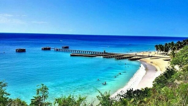 A beach with clear turquoise water, a pier, and a sandy shore lined with palm trees. - #26 Beach Apartment 2br, 3ba w/ jet tub (Isabela)