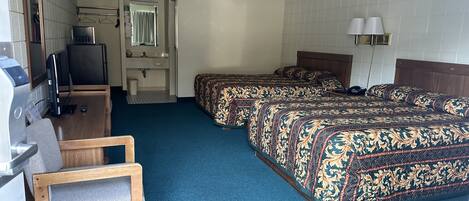 A hotel room with a desk, two beds, a chair, a TV, and a bathroom.