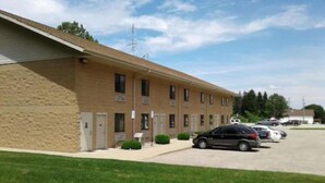 A multi-story building with a beige exterior, several windows, and a parking area with cars. - Oakridge Motel (Newaygo)