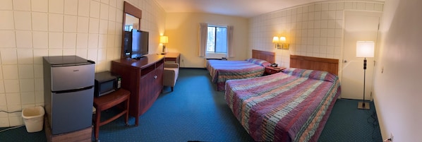 Habitación de hotel con dos camas, un escritorio con refrigerador y microondas, un televisor y una ventana con cortinas.