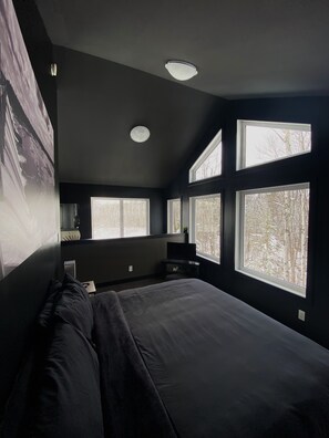 Ein Schlafzimmer mit einem großen Bett, mehreren Fenstern und einer Deckenleuchte.