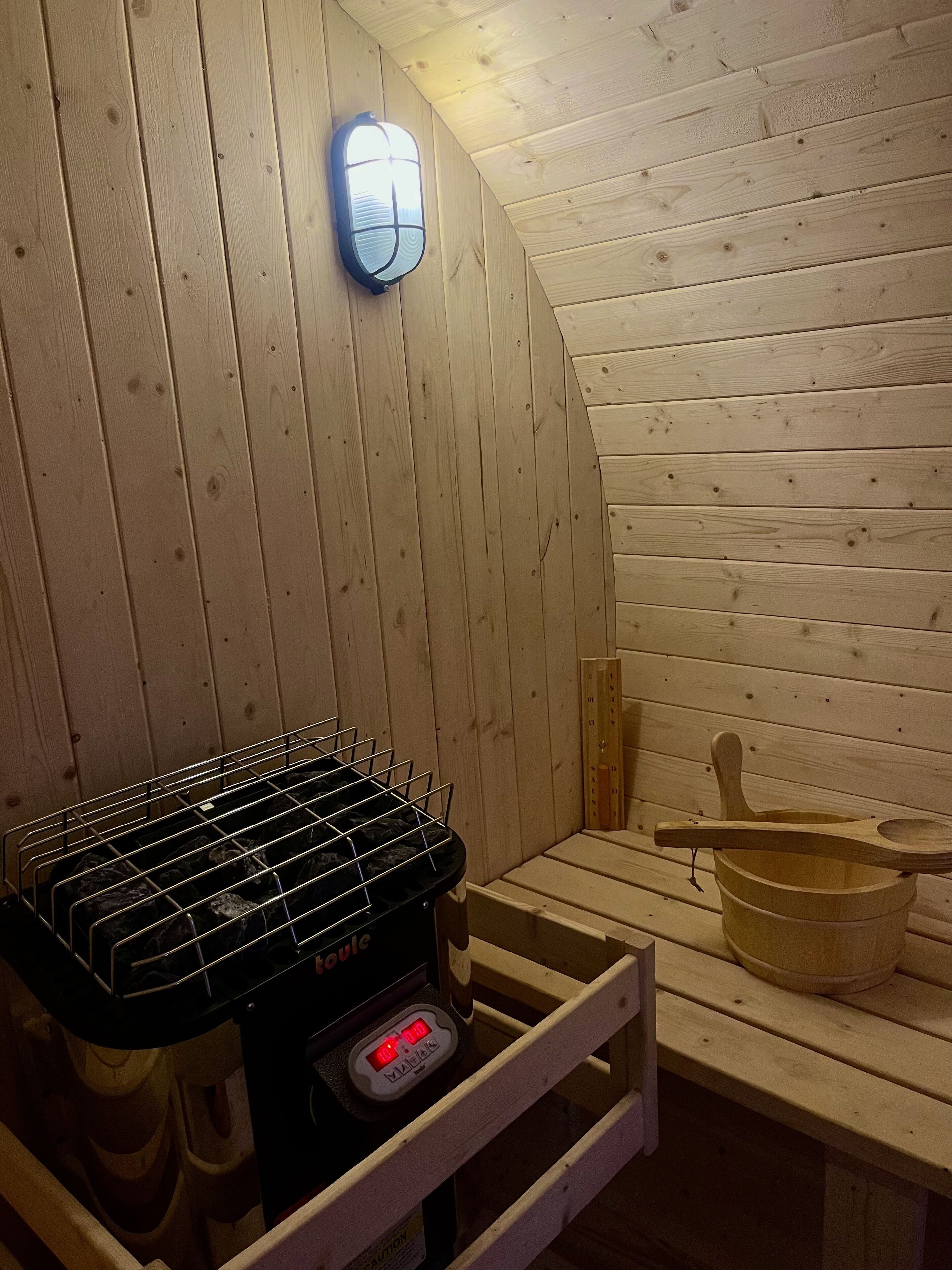 A sauna room with wooden walls, a sauna heater, a wooden bucket, and a wooden spoon.