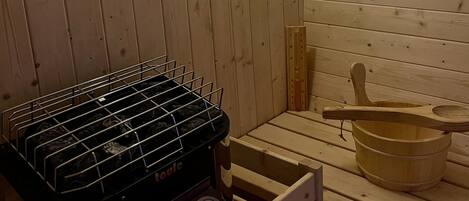 A sauna room with wooden walls, a sauna heater, a wooden bucket, and a wooden spoon.