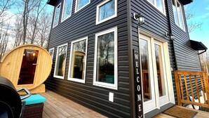 A two-story building with a dark exterior, multiple windows, and a wooden deck. - Romantic Getaway, Tiny High-Rise Cabin (Whitemouth)