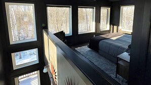 A bedroom with a loft bed, multiple windows, and a ceiling light fixture. - Romantic Getaway, Tiny High-Rise Cabin (Whitemouth)