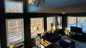 A modern living room with large windows, a fireplace, and a TV. - Romantic Getaway, Tiny High-Rise Cabin (Whitemouth)