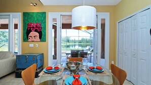 A dining area with a glass table set for six, a blue trunk, and a painting on the wall. - Your Lake Front Hideaway in Paradise Hideaway in Paradise - 7BR Luxurious Villa (Kissimmee)