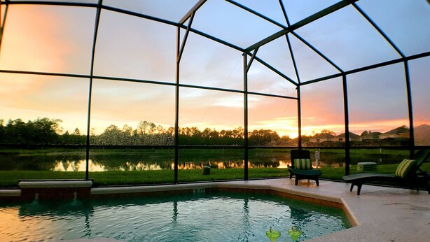 A pool area with a glass enclosure, a chair, and a glass of drink. - Your Lake Front Hideaway in Paradise Hideaway in Paradise - 7BR Luxurious Villa (Kissimmee)