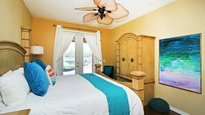 A bedroom with a bed, a wooden wardrobe, a ceiling fan, a painting, and a view through a window. - Your Lake Front Hideaway in Paradise Hideaway in Paradise - 7BR Luxurious Villa (Kissimmee)