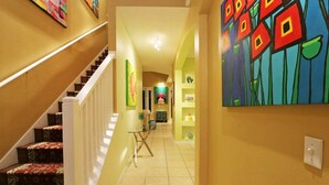 A hallway with a staircase, a glass table, and colorful artwork on the walls. - Your Lake Front Hideaway in Paradise Hideaway in Paradise - 7BR Luxurious Villa (Kissimmee)