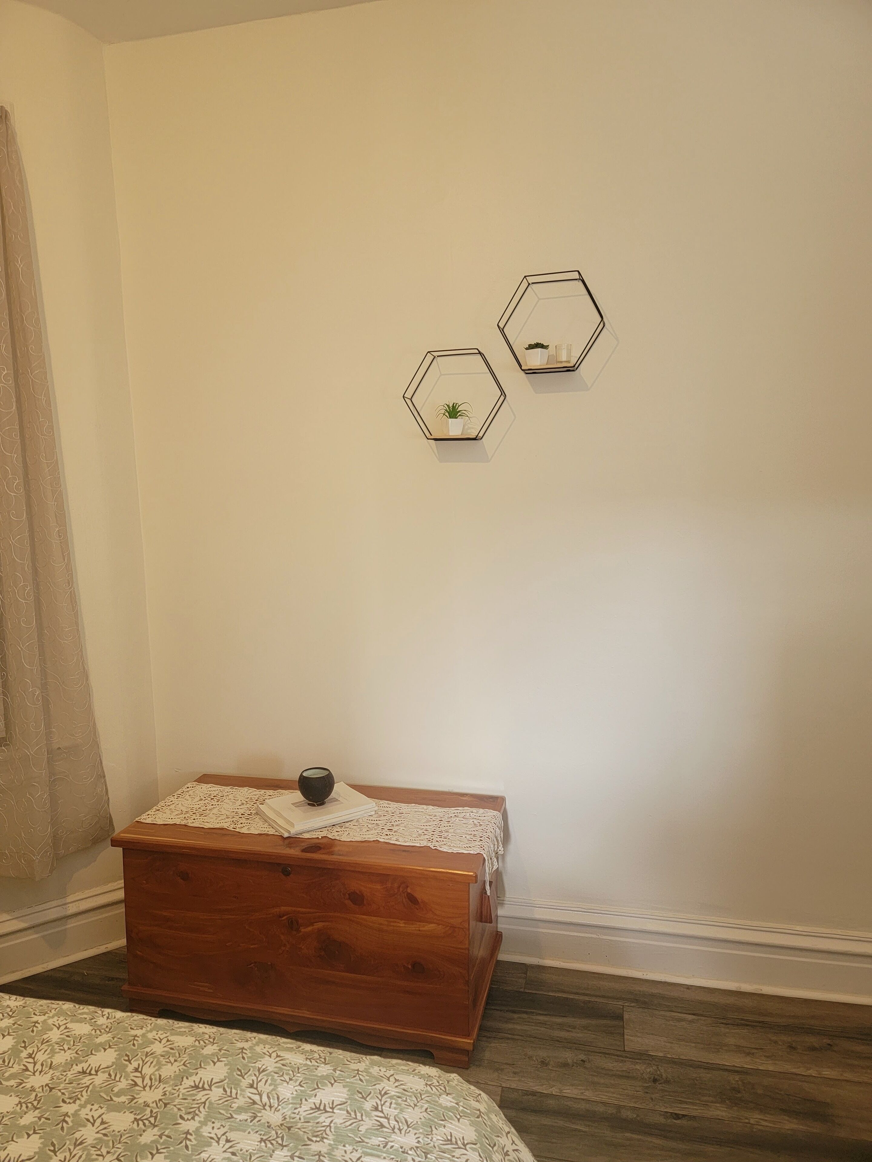 Quarto com uma cômoda de madeira, colcha estampada e duas decorações hexagonais na parede.