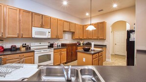 A kitchen with wooden cabinets, a microwave, stove, sink, and a hanging light fixture. - Private Pool & Spa | Rare Wooded View | Minutes to Disney | Game Room & BBQ ⭐ Best overall (Kissimmee)