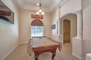 Une table de billard avec un placage en bois, un luminaire au plafond et une porte visible au fond.