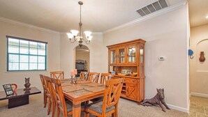 A dining room with a wooden table and chairs, a chandelier, a cabinet with glass doors, and a decorative horse sculpture. - Private Pool & Spa | Rare Wooded View | Minutes to Disney | Game Room & BBQ ⭐ Best overall (Kissimmee)