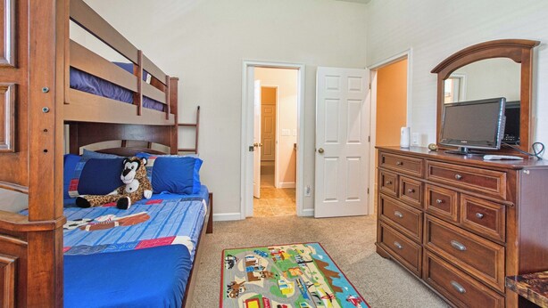 A bedroom with a bunk bed, a dresser, a television, and a door leading to another room. - Private Pool & Spa | Rare Wooded View | Minutes to Disney | Game Room & BBQ ⭐ Best overall (Kissimmee)