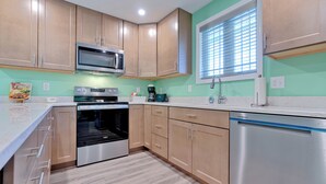A modern kitchen with wooden cabinets, stainless steel appliances, and a window with blinds.