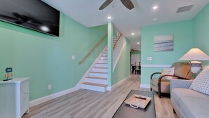 A living room with a staircase, a TV mounted on the wall, a lamp, and a sofa.