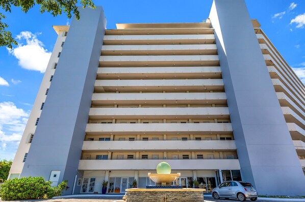 A multi-story hotel with a central fountain, a clear blue sky, and a parked car.