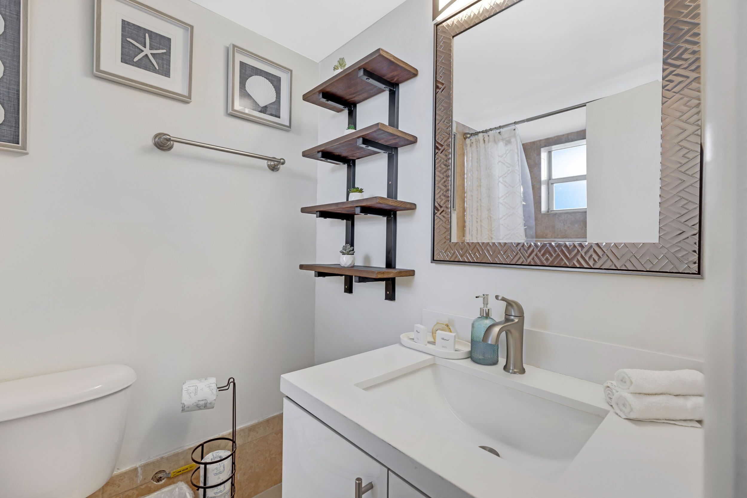 A bathroom with a white sink, a mirror with a decorative frame, and a towel rack.
