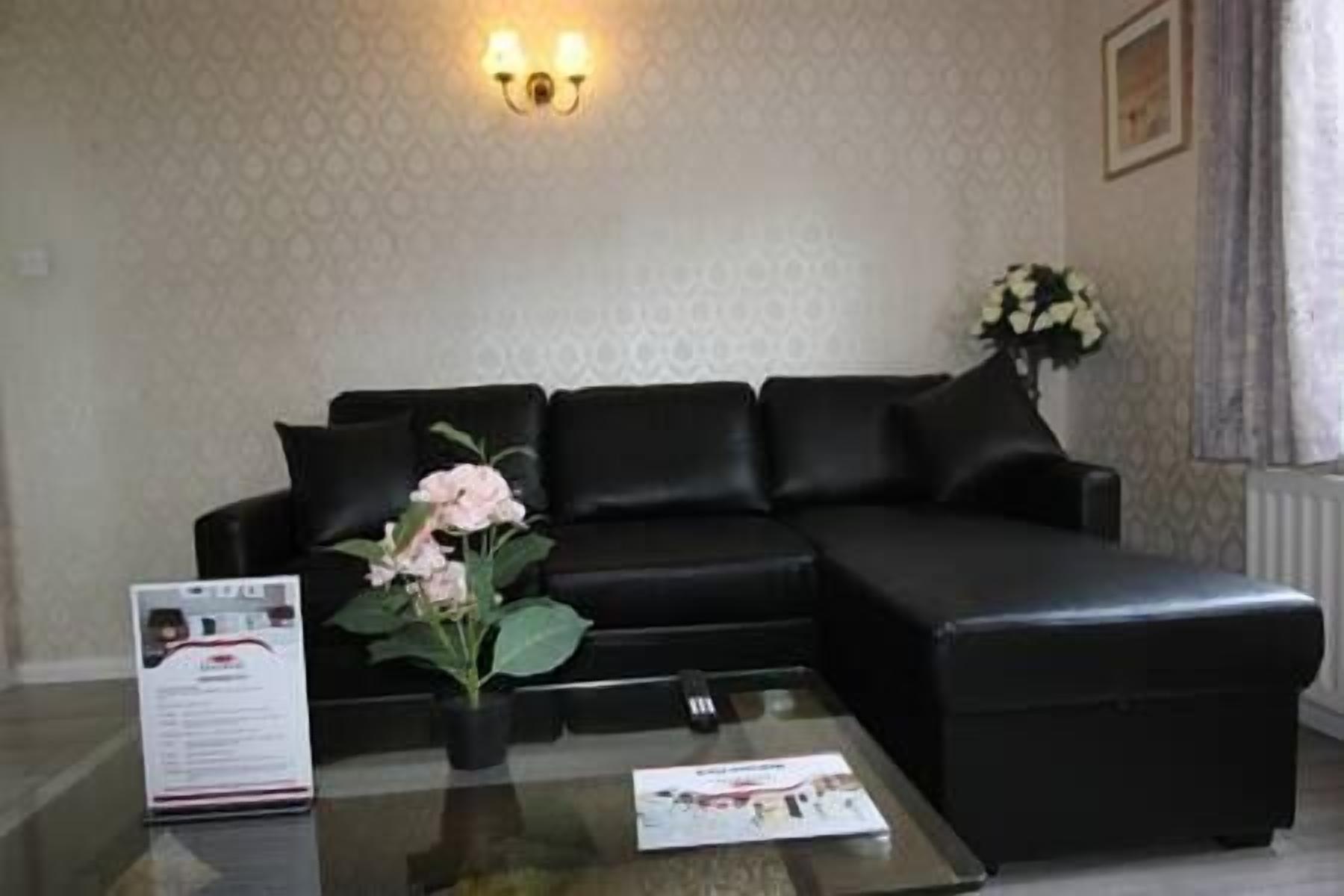 A black leather sofa with a floral arrangement on a glass table, a framed picture on the wall, and a light fixture above.