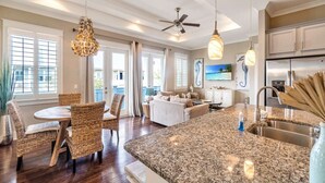 A spacious living area with a dining table, wicker chairs, a sofa, and a kitchen with granite countertops and stainless steel appliances. - TaDa! - Heated Pool and Golf Cart! (Santa Rosa Beach)