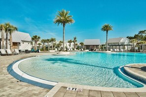 Una piscina con sillas de descanso, palmeras y un cielo azul despejado.