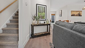 Eine Treppe mit hölzernem Geländer, ein Konsolentisch mit Dekoration, ein graues Sofa und ein gerahmtes Bild an der Wand.