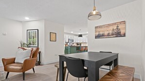 Ein moderner Essbereich mit einem dunklen Holztisch, schwarzen Stühlen und einer Sitzbank mit Fischgrätmuster. Eine Pendelleuchte hängt über dem Tisch, und ein gerahmtes Bild ist an der Wand.