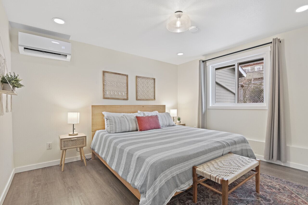 A bedroom with a bed, bedside tables, a window, and an air conditioning unit.