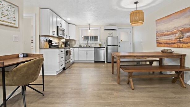 A modern kitchen with white cabinets, stainless steel appliances, and a wooden dining table. - Upscale Rockwood Boho Townhouse (Spokane)