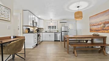 A modern kitchen with white cabinets, stainless steel appliances, and a wooden dining table.