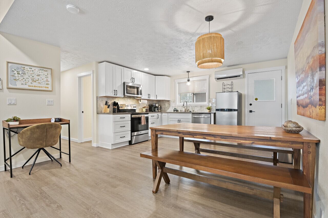 A modern kitchen with white cabinets, stainless steel appliances, and a wooden dining table.