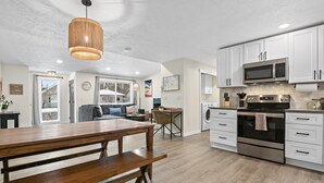 A modern kitchen with white cabinets, stainless steel appliances, and a wooden dining table. - Upscale Rockwood Boho Townhouse (Spokane)