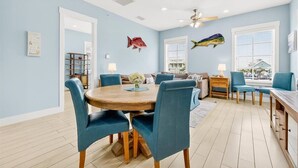 A dining area with a round wooden table, blue upholstered chairs, and a ceiling fan. - South Pier TC 3201 (Port Aransas)