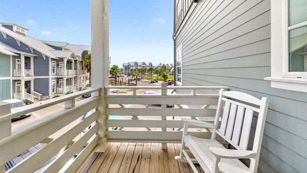 A wooden deck with white railings and benches, overlooking a street with buildings and parked cars. - South Pier TC 3201 (Port Aransas)