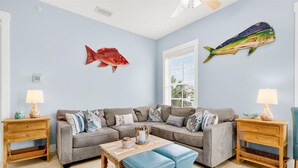 A living room with a grey sofa, blue ottoman, wooden coffee table, and two nightstands with lamps. - South Pier TC 3201 (Port Aransas)