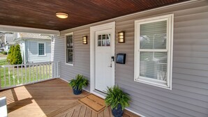 Un porche abrité avec un plancher en bois, une porte blanche et deux plantes en pot.