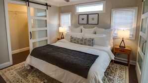 Une chambre à coucher comprenant un lit, deux tables de chevet avec des lampes, un ventilateur de plafond et un placard à portes coulissantes.