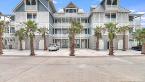 A large, multi-story building with a symmetrical facade, multiple balconies, and a parking area with several cars. - Beach Craft TC 8202 (Port Aransas)