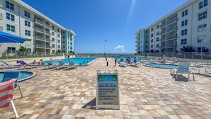 A pool area with lounge chairs, a sign with pool rules, and a view of the ocean. - Ground Floor Beachfront Complex Unit w/Pool & Beach Access (New Smyrna Beach)